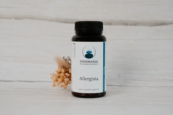 Eine schwarze Flasche mit einem weiß-blauen Etikett steht auf einer hellen Holzoberfläche. Beigefarbene Trockenblumen sind neben der Flasche platziert.